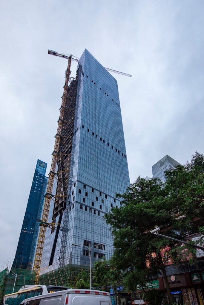Modern skyscraper under construction with cranes in a bustling urban area.
