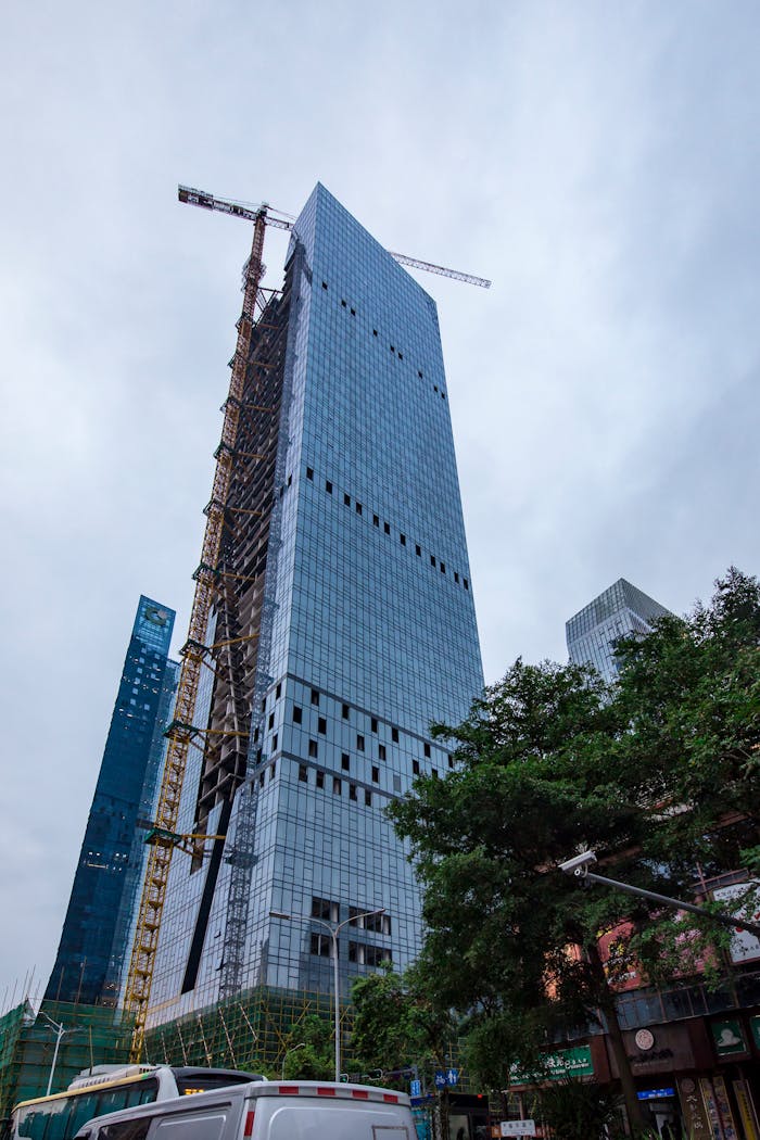Modern skyscraper under construction with cranes in a bustling urban area.